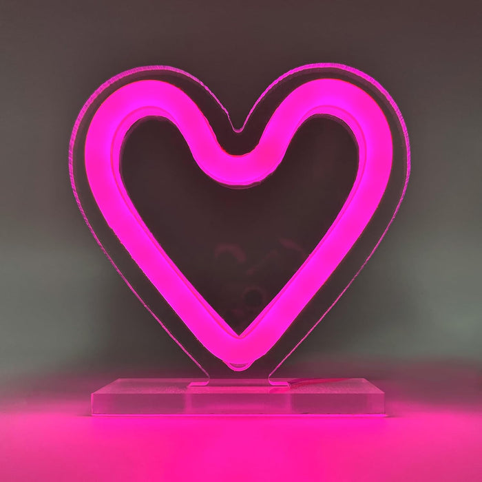 Luz LED decorativa en forma de corazón con efecto neón rosa y base estable.